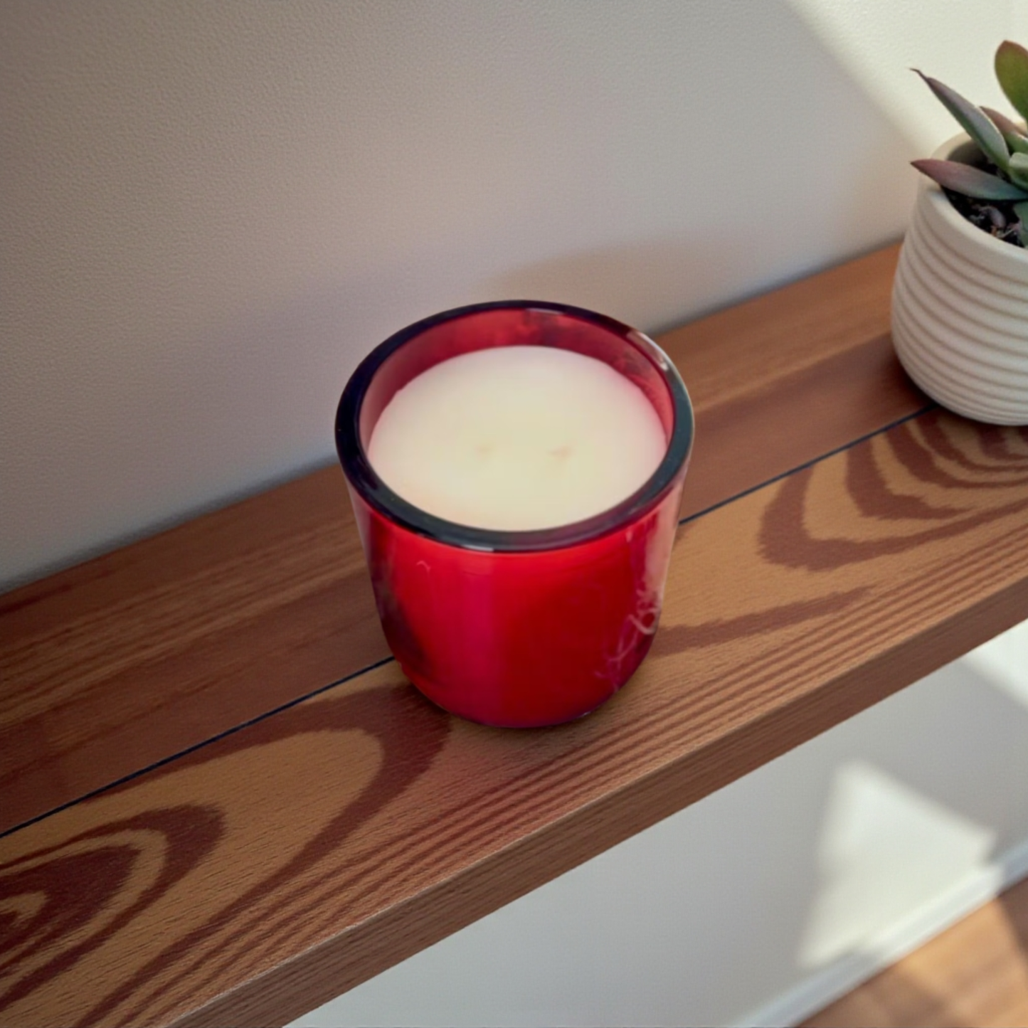 Winter Reigns red glass candle vessel on a wooden shelf with a succulent plant next to it