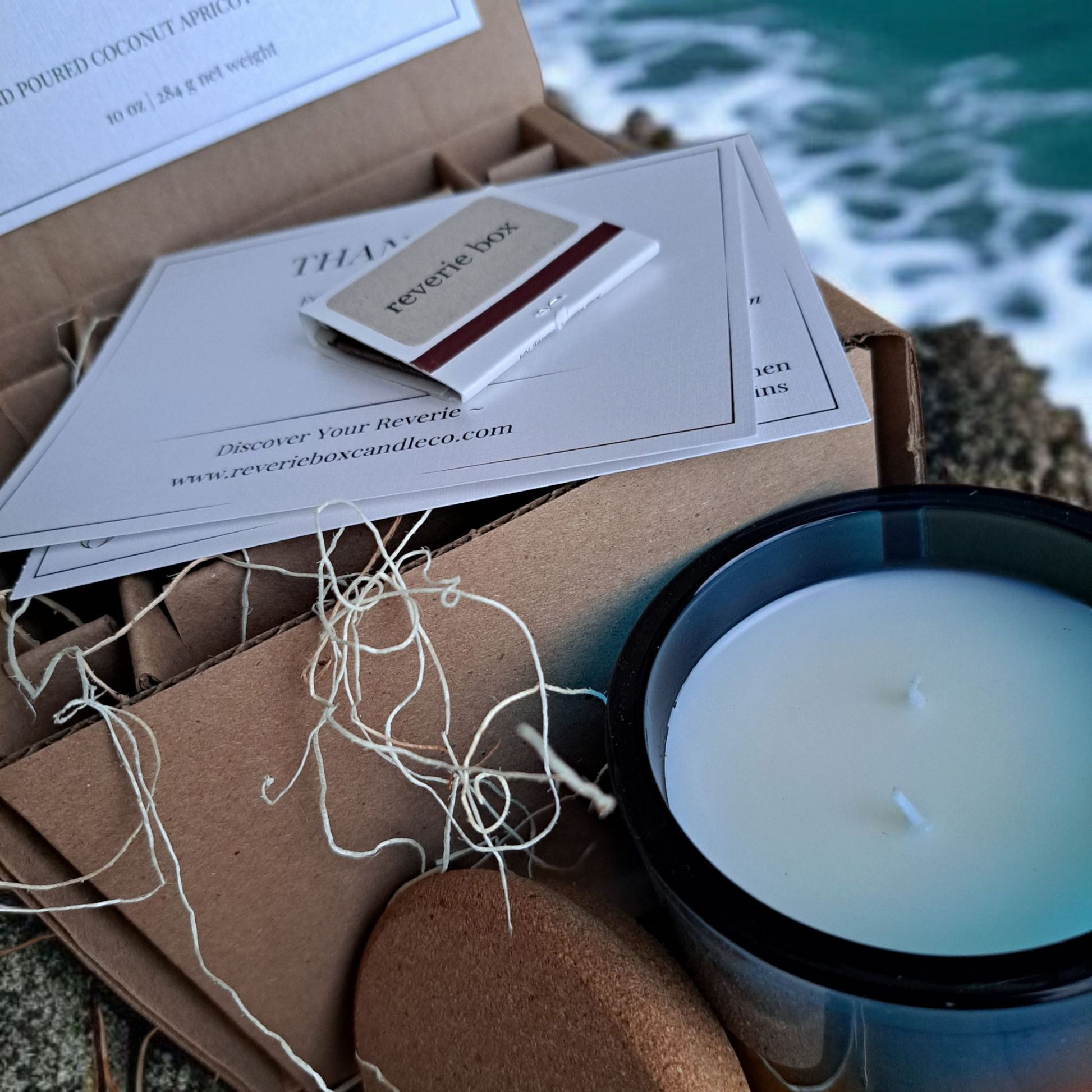 Saltmere candle and box with cards on rocky beach shore