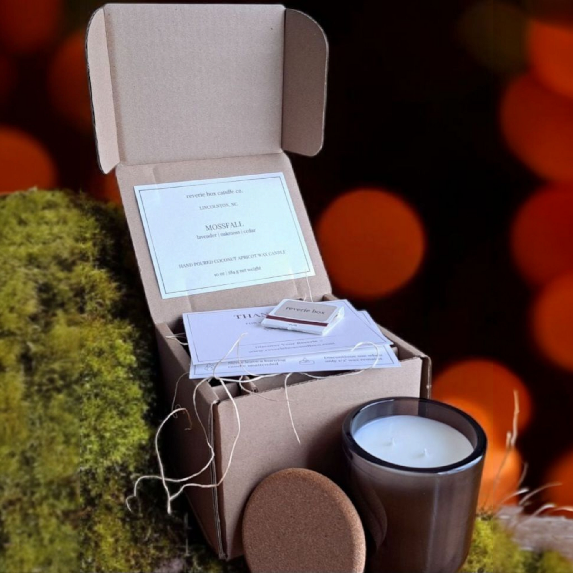 Open cardboard box with Mossfall candle and product cards with blurred natural background