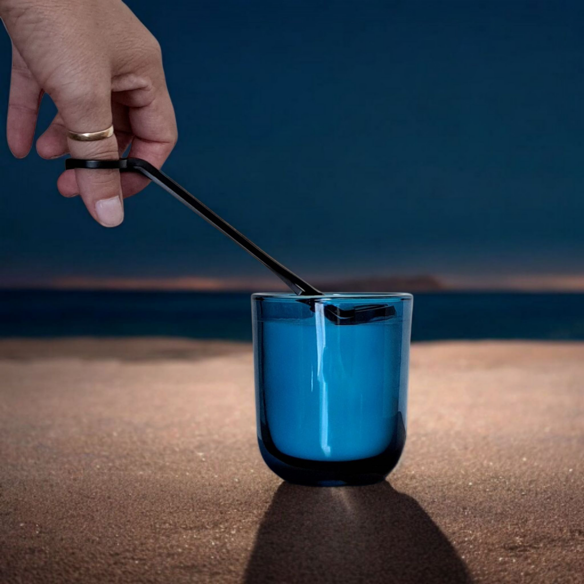 Hand trimming Saltmere candle wick in blue jar on dark beach