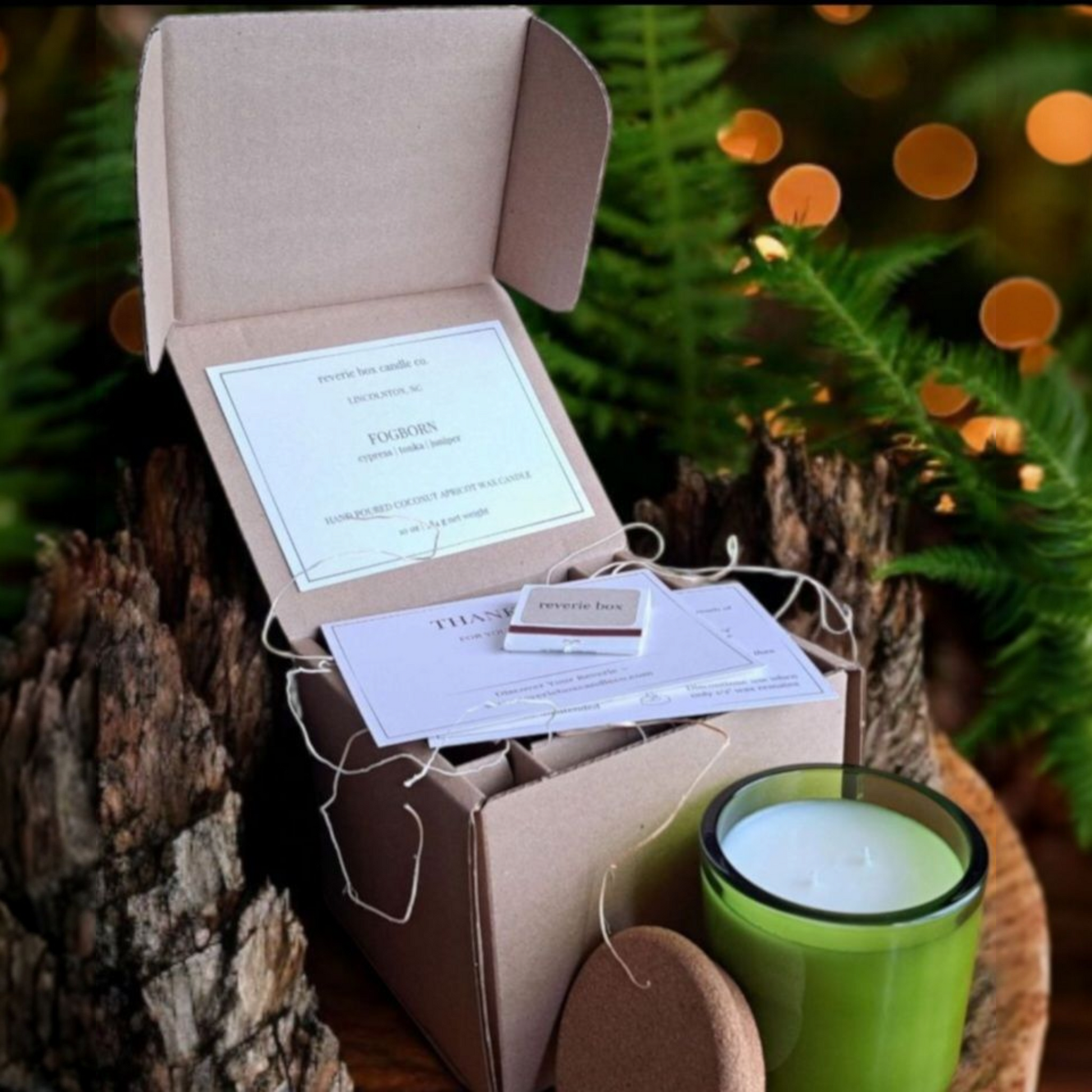 Fogborn candle and box with product cards against dark forest background