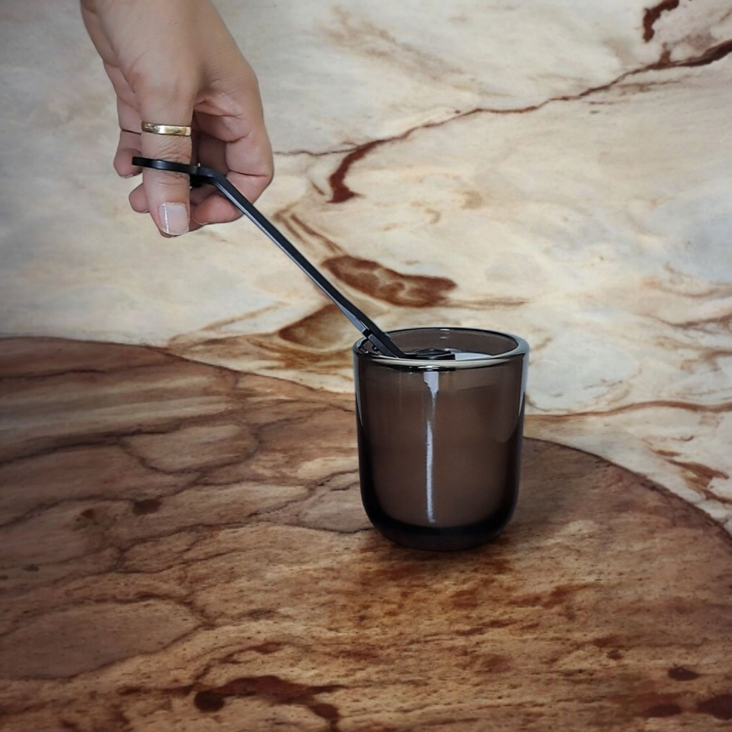 Person trimming Mossfall candle wick in amber tumbler on marbled surface