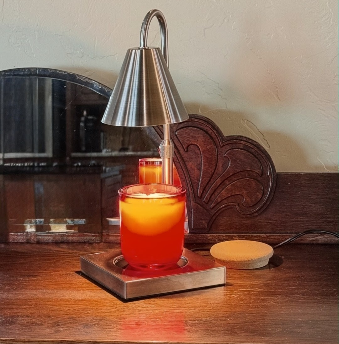 A Reverie Box Winter Reigns candle glowing beneath a silver candle warmer lamp on a dark wood dresser