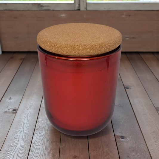 Winter Reigns red glass vessel with cork lid on smooth wooden slat surface