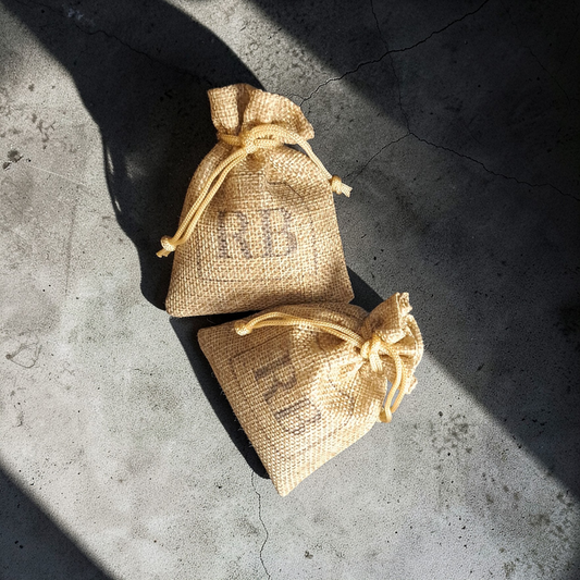 Two small beige Reverie Box drawstring scent sachets on a concrete surface with shadows cast by the bags.