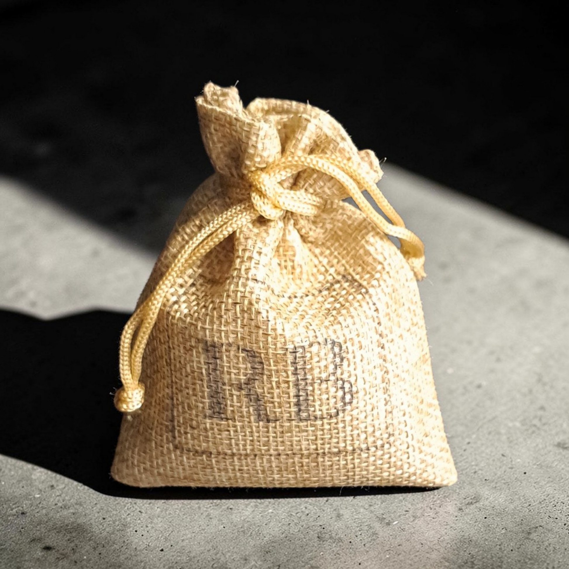 Smooth burlap bag with RB branding, sitting on a concrete surface with light and shadows.
