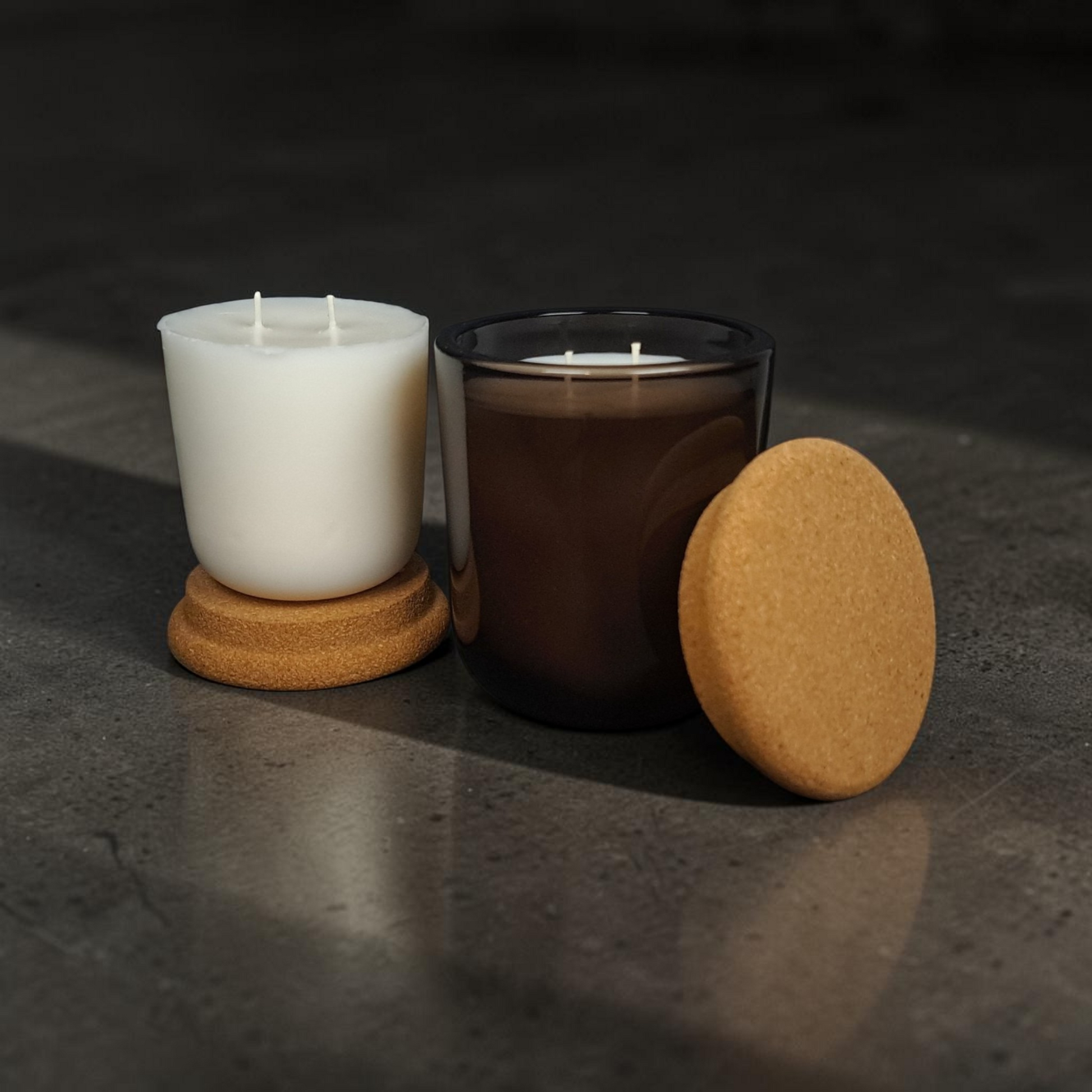 A stand alone coconut apricot wax candle refill insert showing smooth wax detail and double wicks sitting next to Mossfall smoke brown glass candle with cork lid. 