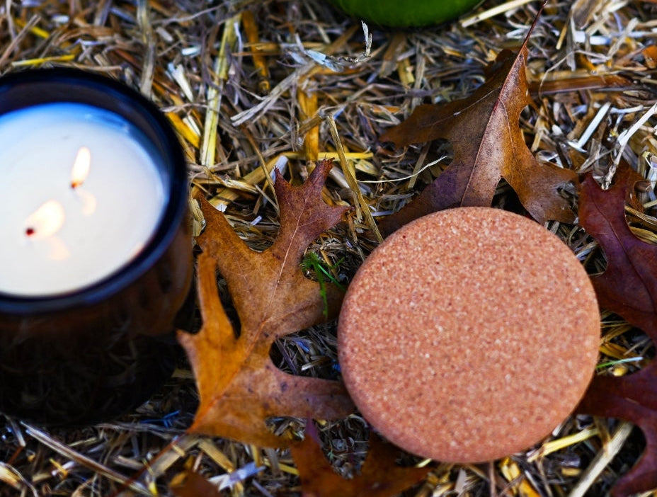 lit brown glass candle with cork lid and leaves on hay bale