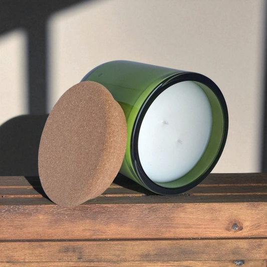 Close-up of Fogborn green glass candle tilted to show smooth wax surface and double wicks with natural cork lid on rustic wooden surface