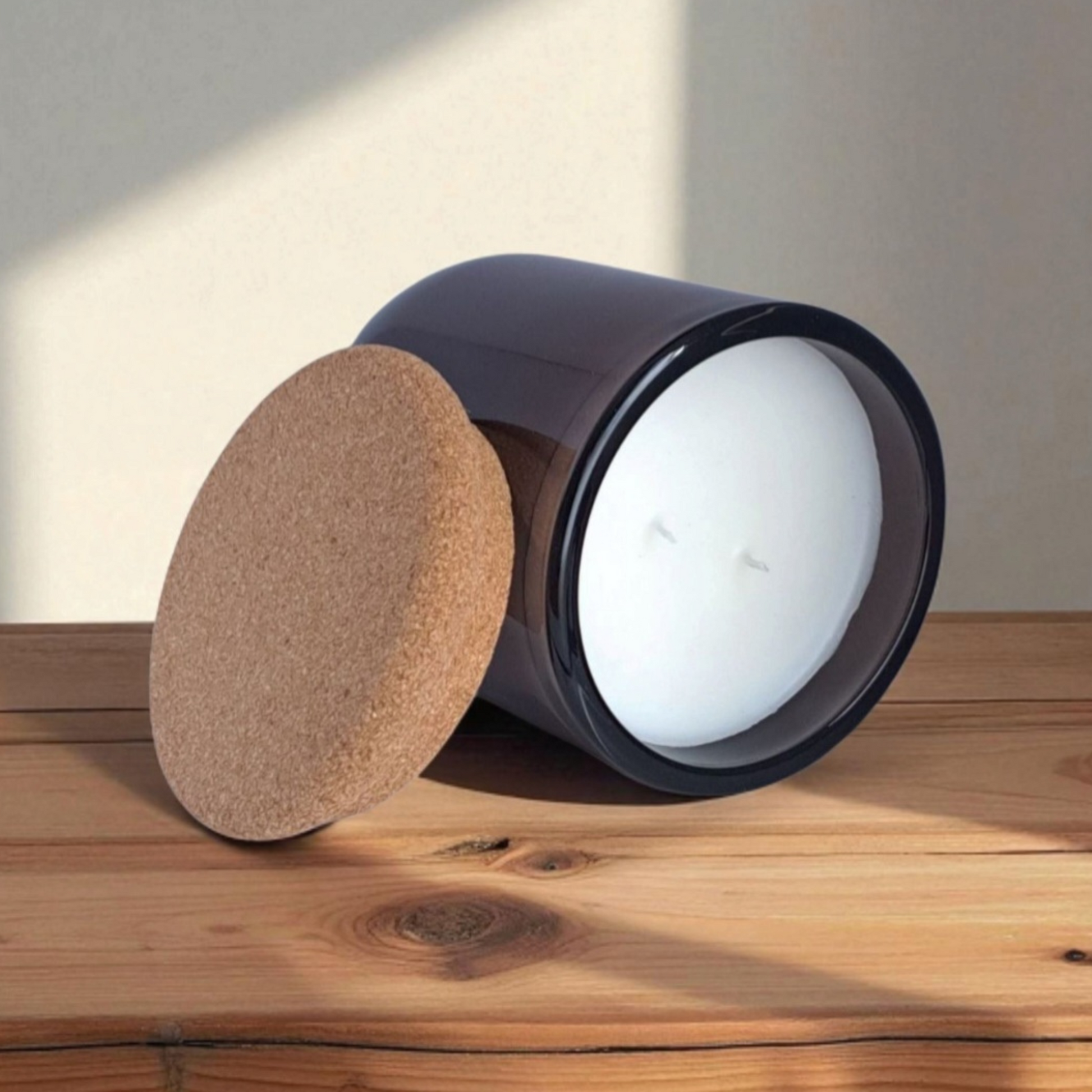 Mossfall candle in brown glass tilted to show natural cork lid and smooth wax surface with double wicks on wooden surface