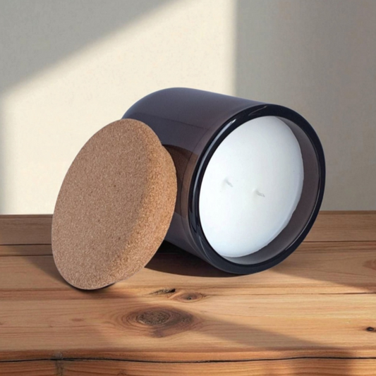 Mossfall candle in brown glass tilted to show natural cork lid and smooth wax surface with double wicks on wooden surface