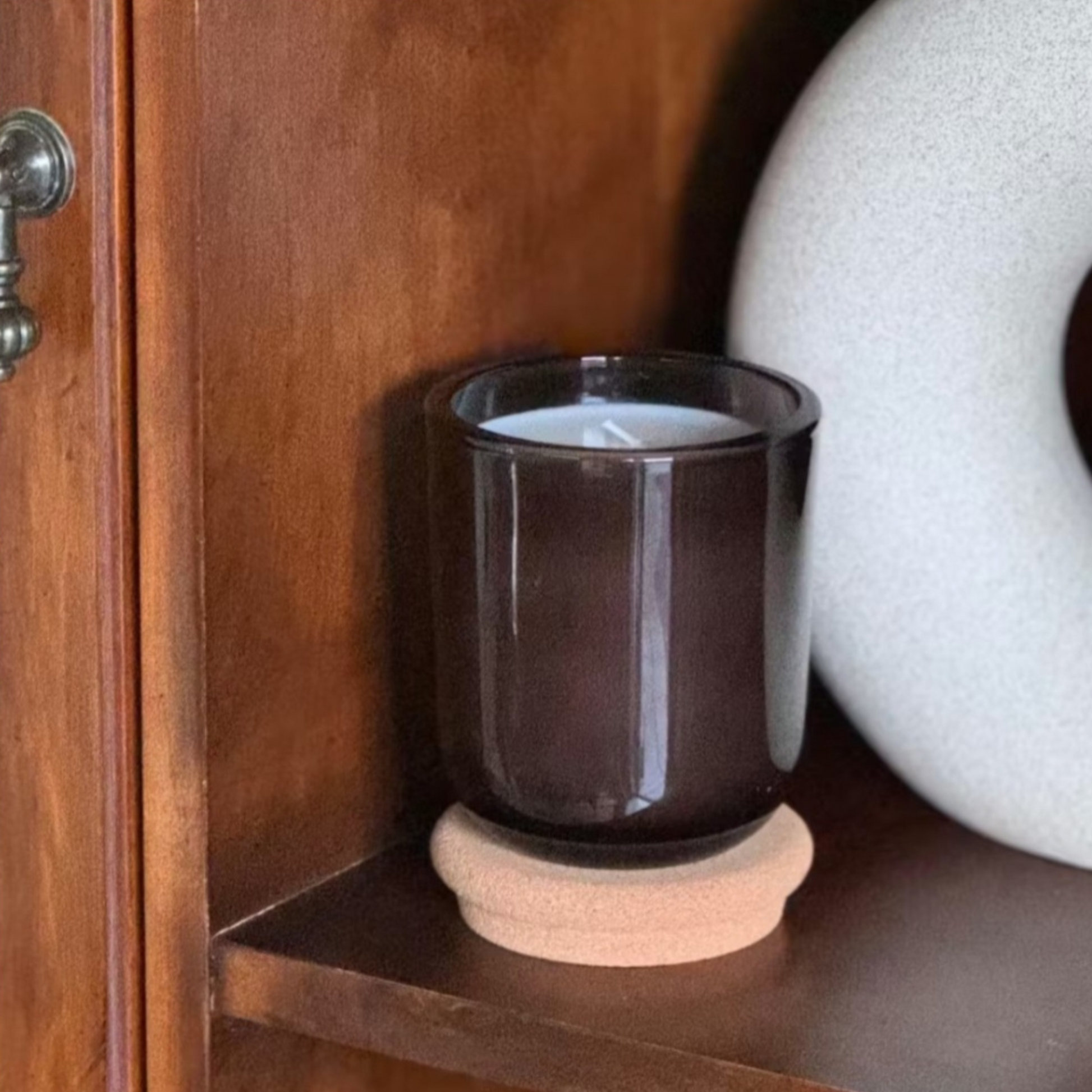 Mossfall brown glass candle with cork lid on wooden shelf next to white ceramic vase in minimalist interior